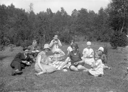 Svartvitt foto från 1931. personer sitter och har picknick i gräset.